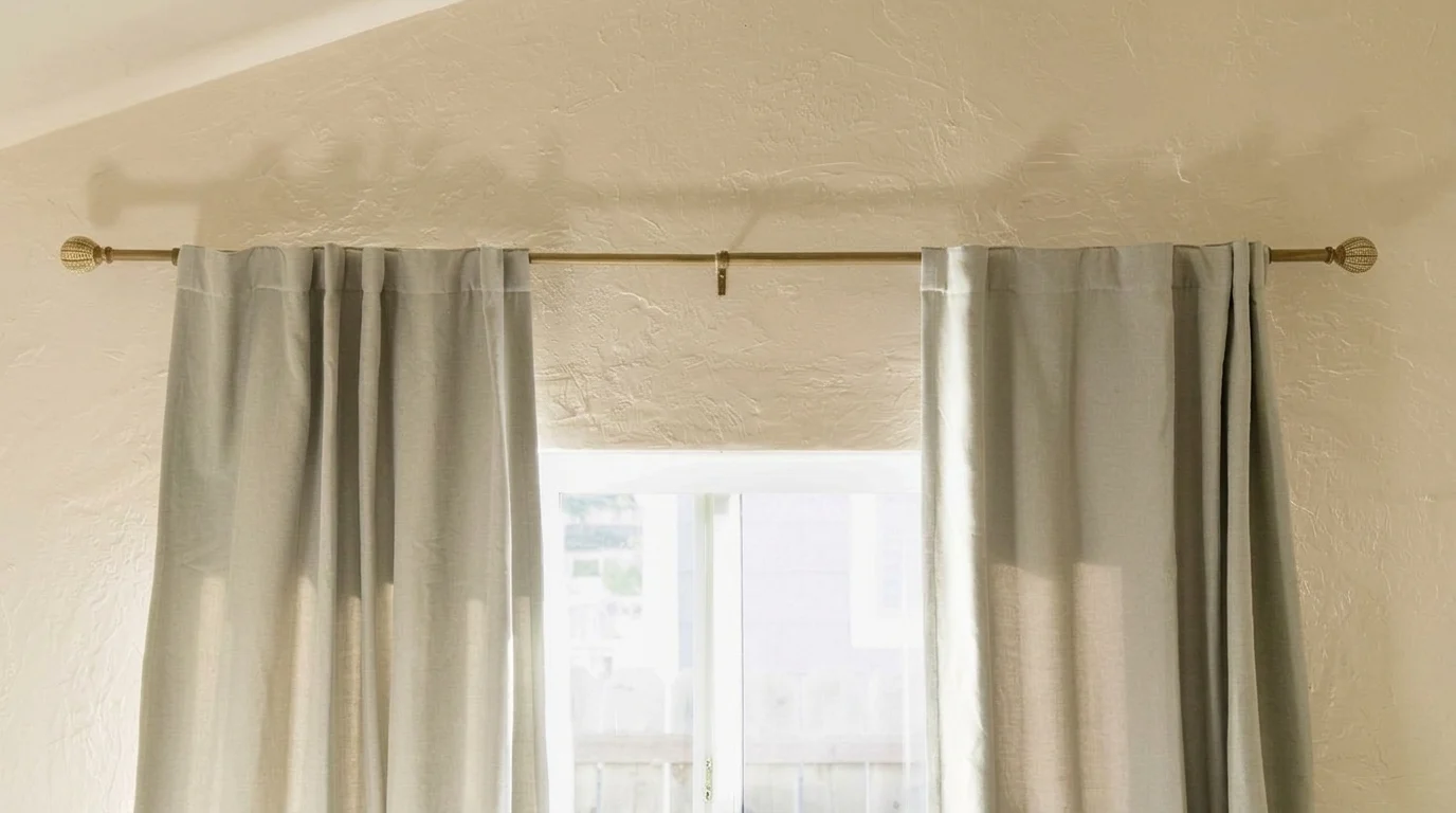 Close-up of a silver metal curtain rod bracket screwed into the wall above white trim.