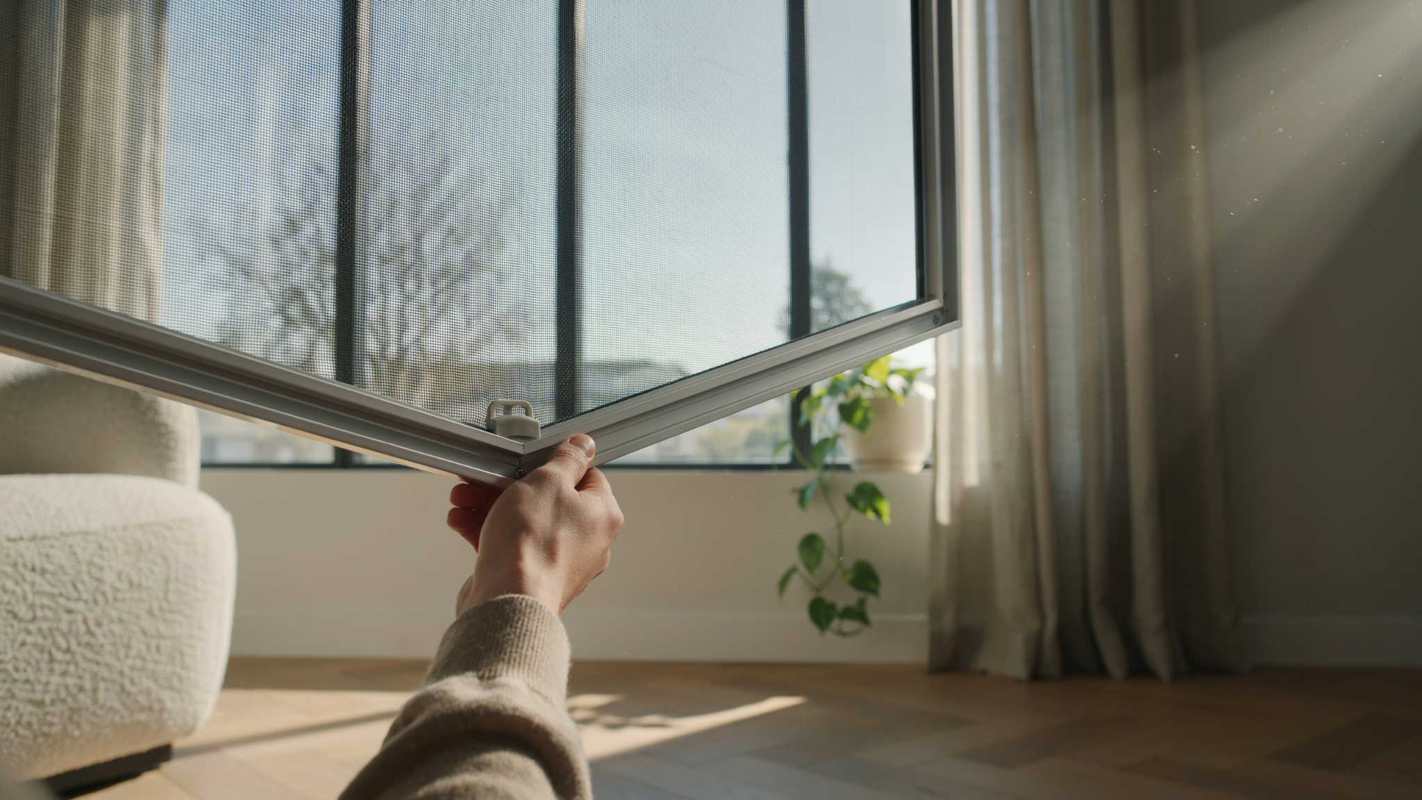 "Close-up of a window screen partially removed from a frame in a modern home, showing mesh detail and hands preparing for maintenance."