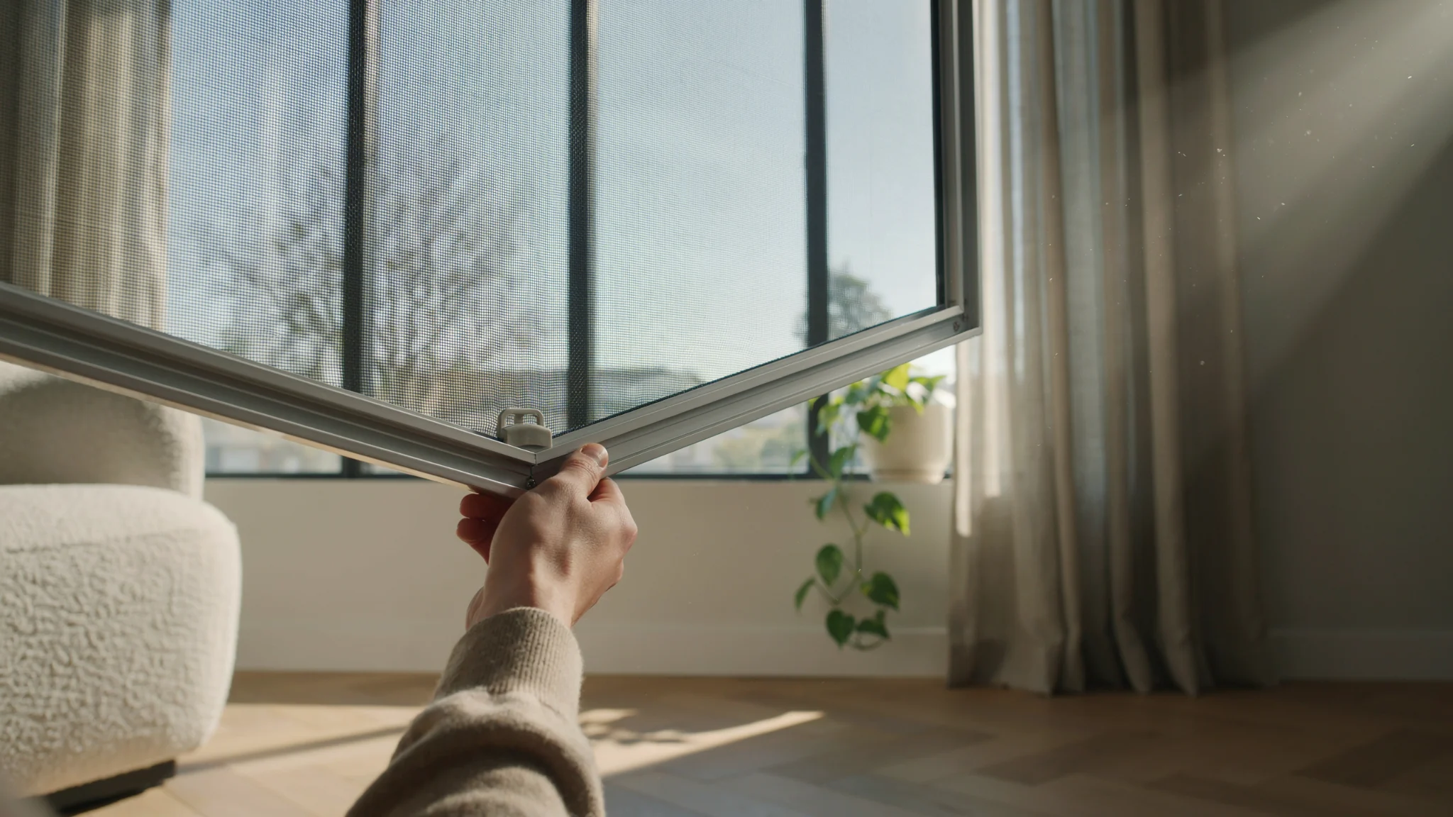 "Close-up of a window screen partially removed from a frame in a modern home, showing mesh detail and hands preparing for maintenance."