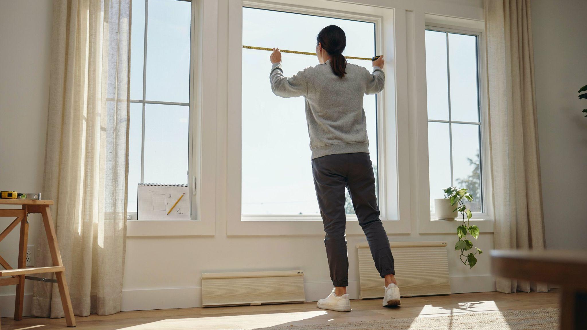 Measuring three windows in a row for accurate blind sizing and installation.