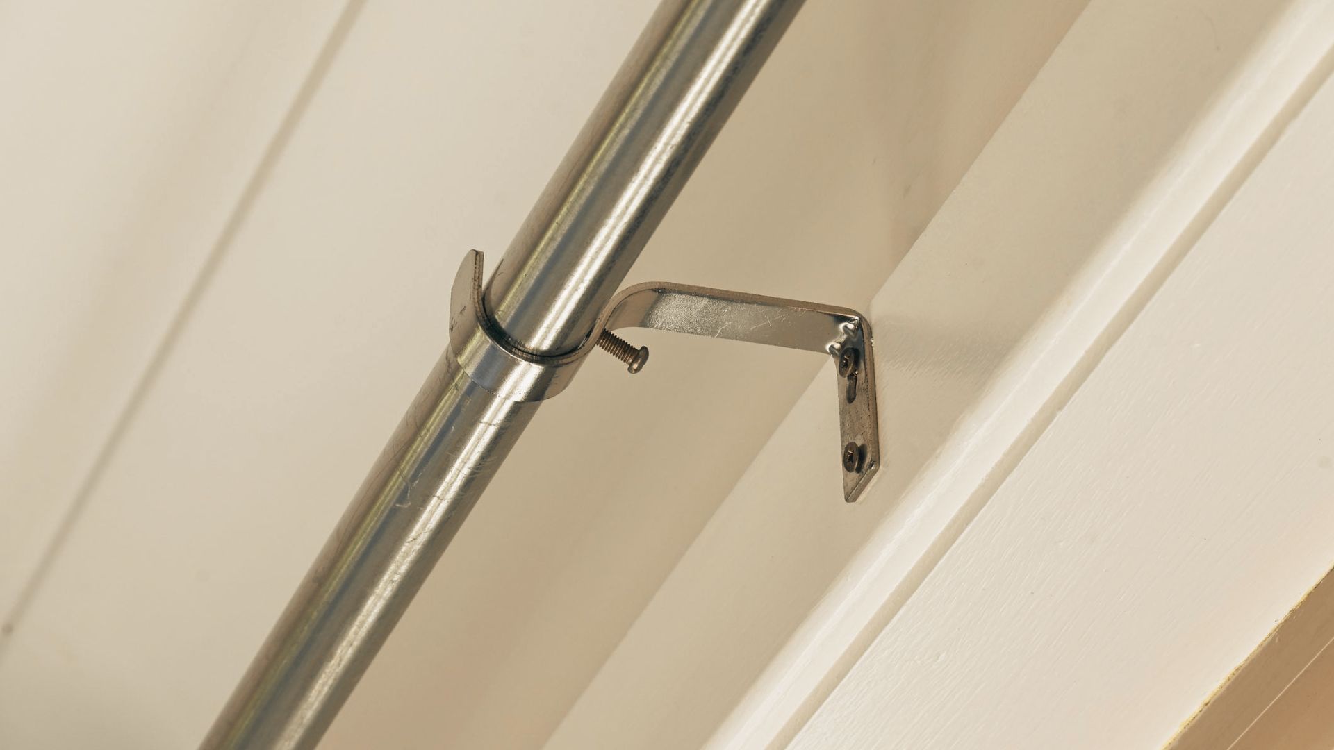 Brass curtain rod with decorative finials mounted several inches above a window frame.