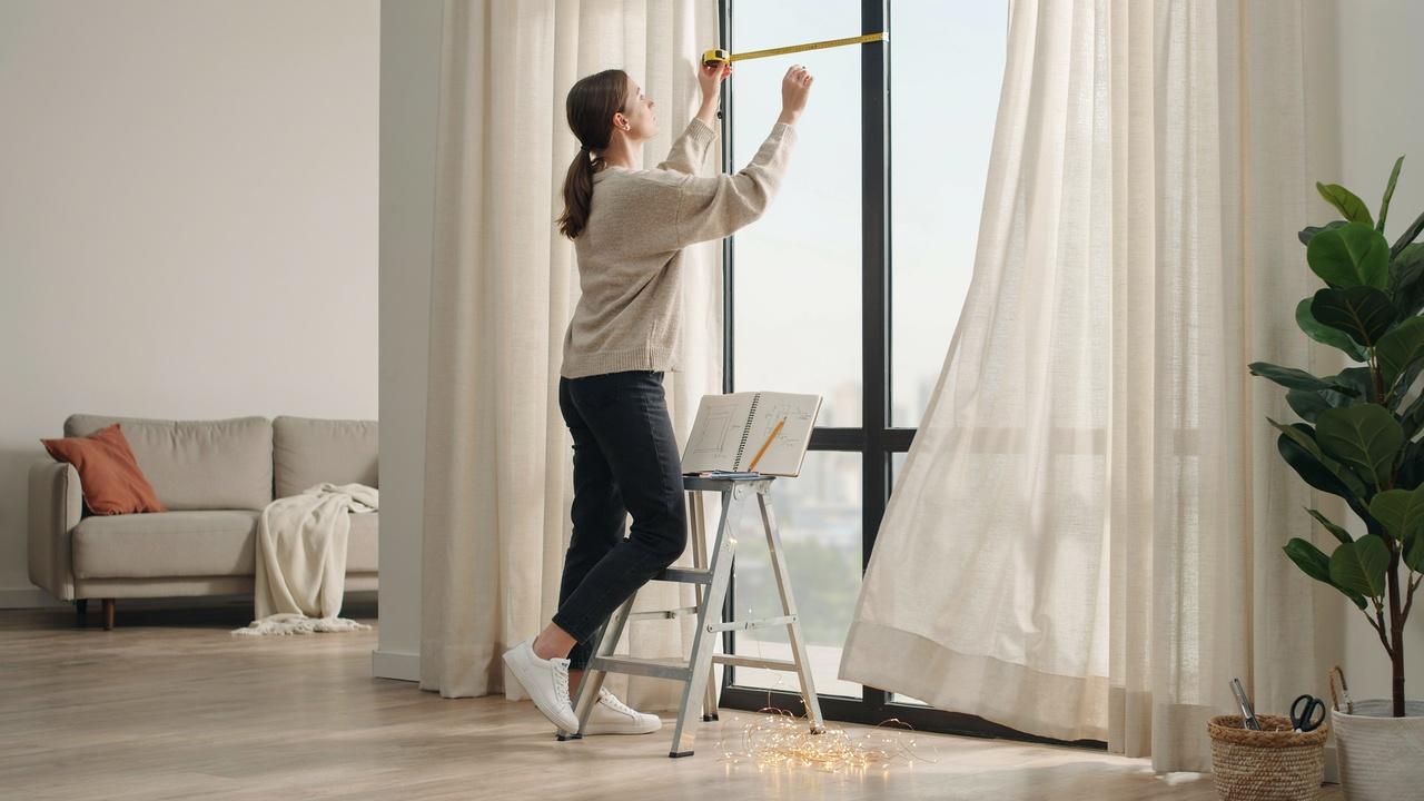 A person measuring a window and planning the installation area before hanging curtain lights.
