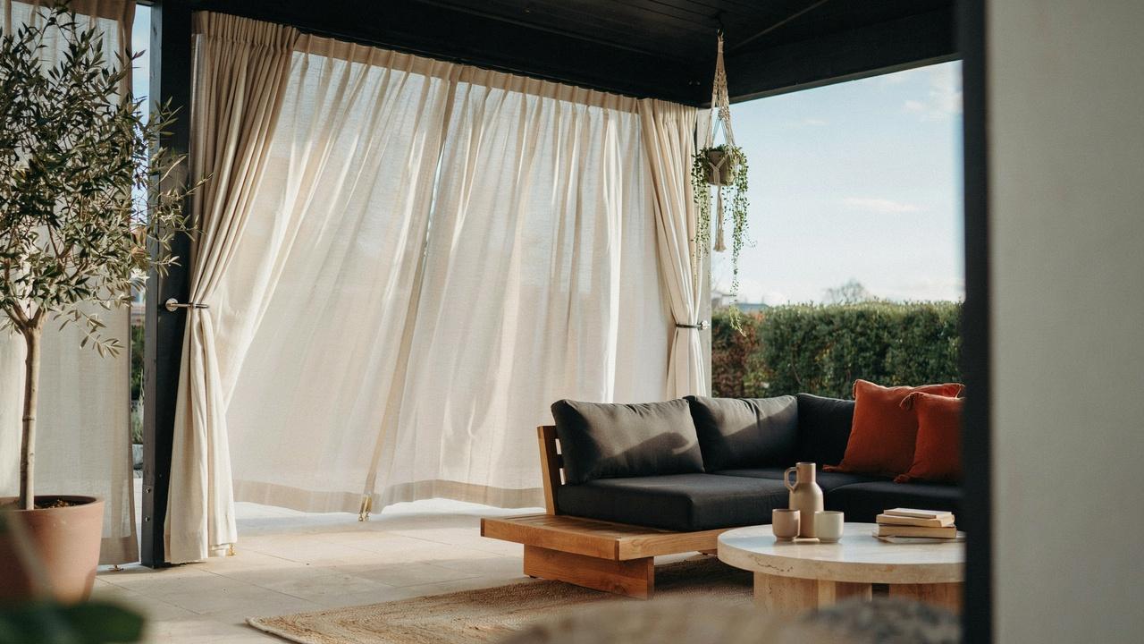 Homeowner adjusting outdoor curtains for a smooth and secure fit on a patio curtain rod.