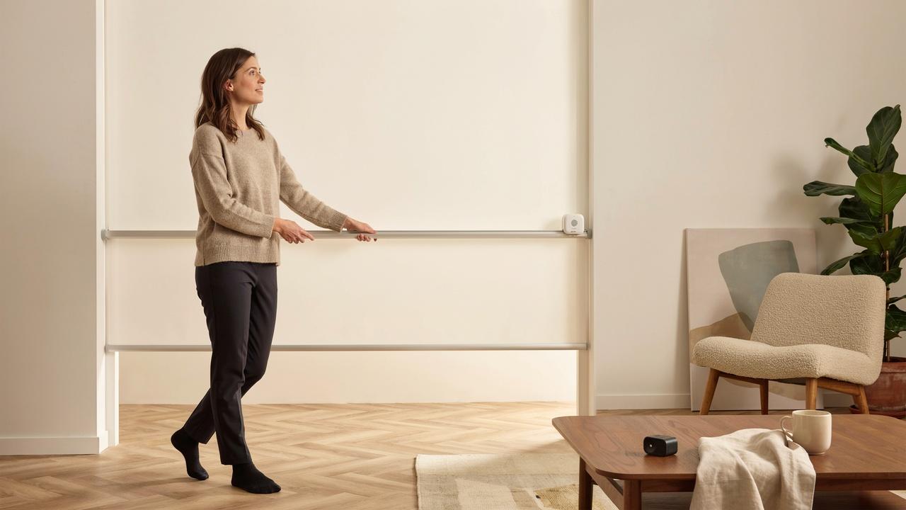 A homeowner gently trying to adjust motorized blinds by hand while a remote control rests nearby.