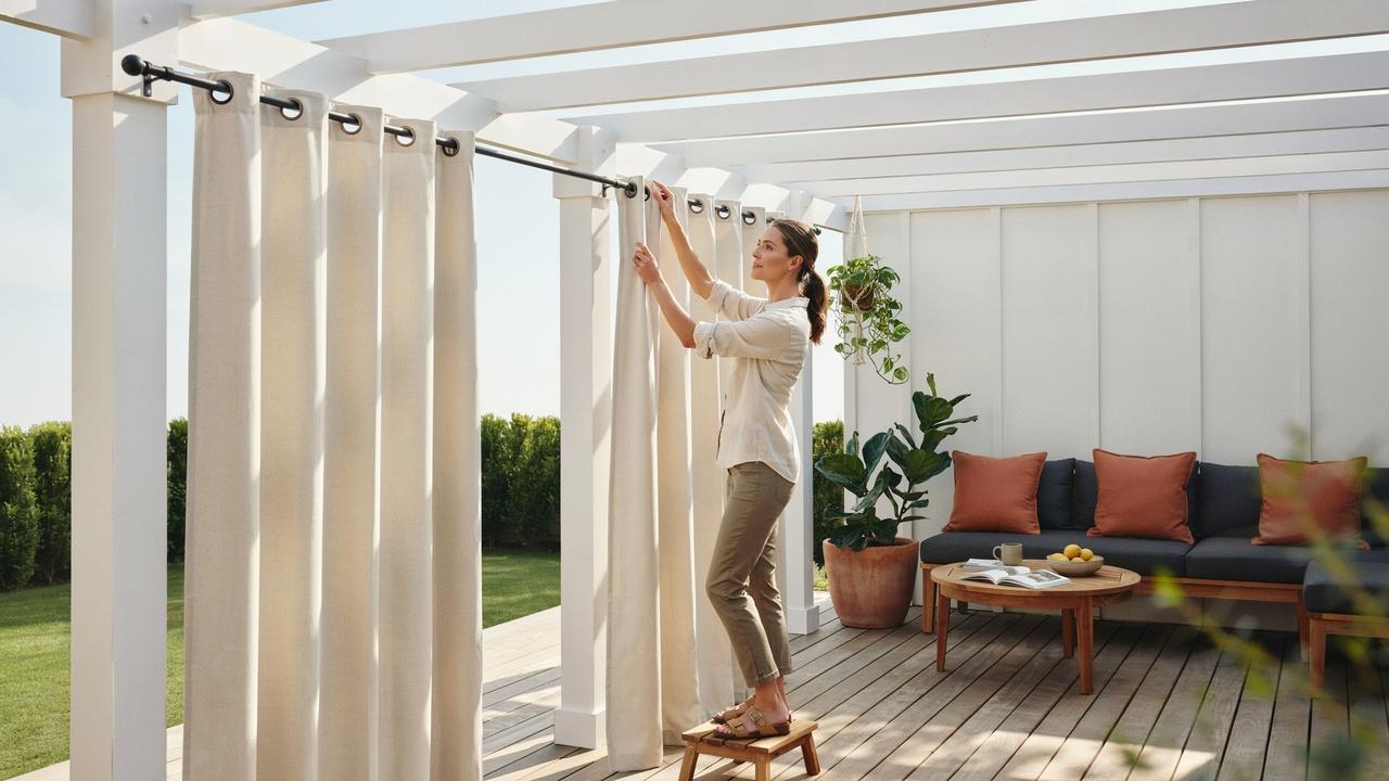 Homeowner securely installing curtain rods and mounting hardware for outdoor curtains on a patio.