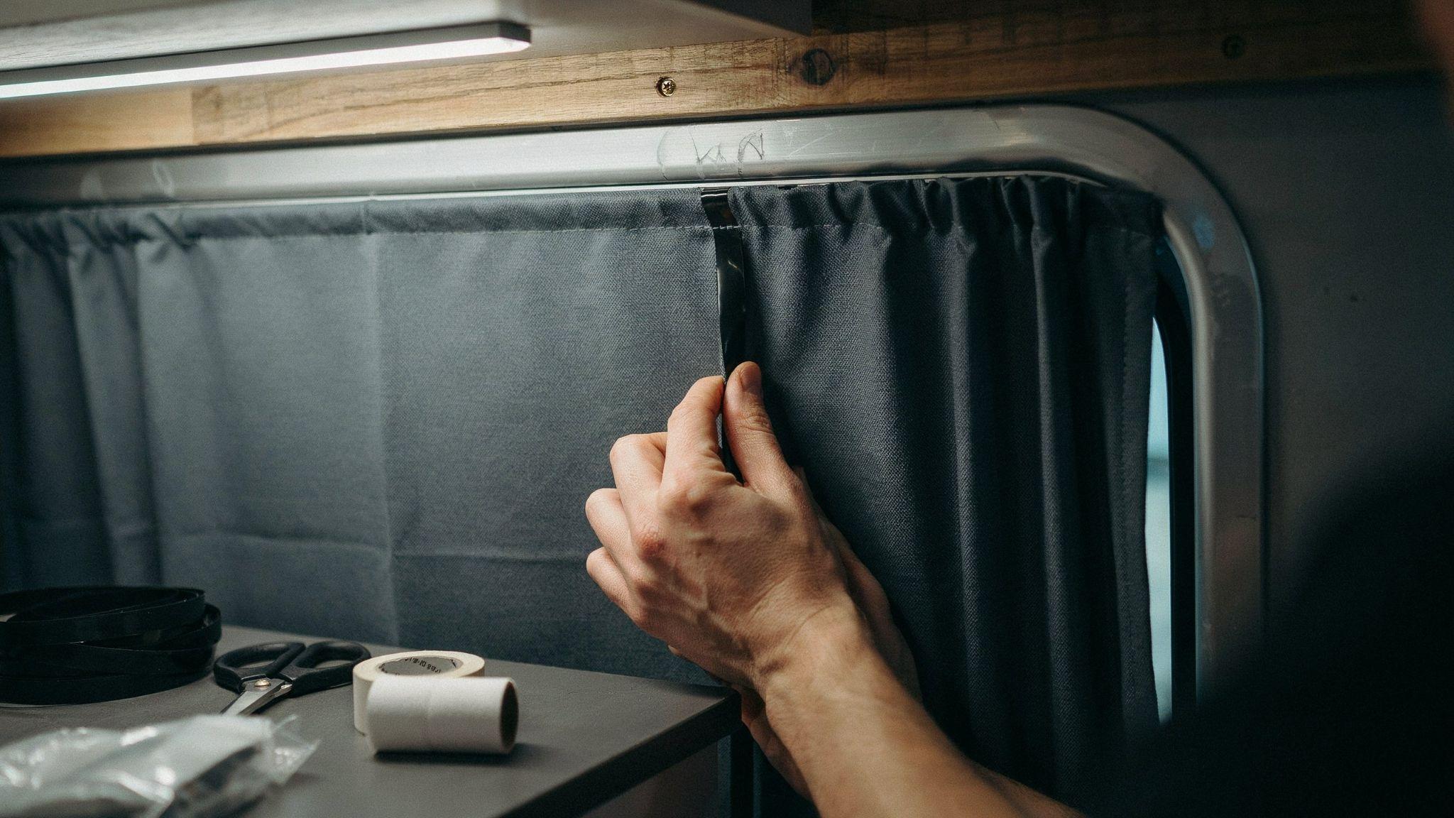 Hand pressing blackout curtain onto camper window frame using adhesive Velcro strips for privacy