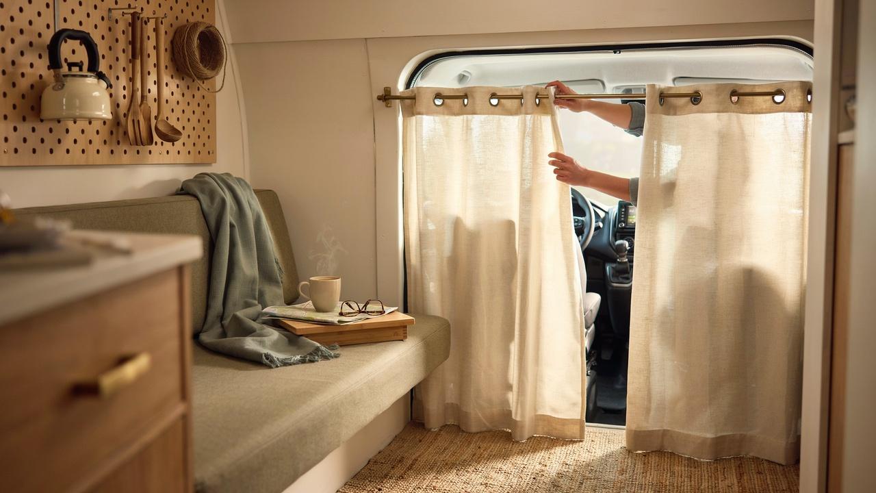 Person sliding beige grommet curtains on a brass rod to separate camper cab from living space