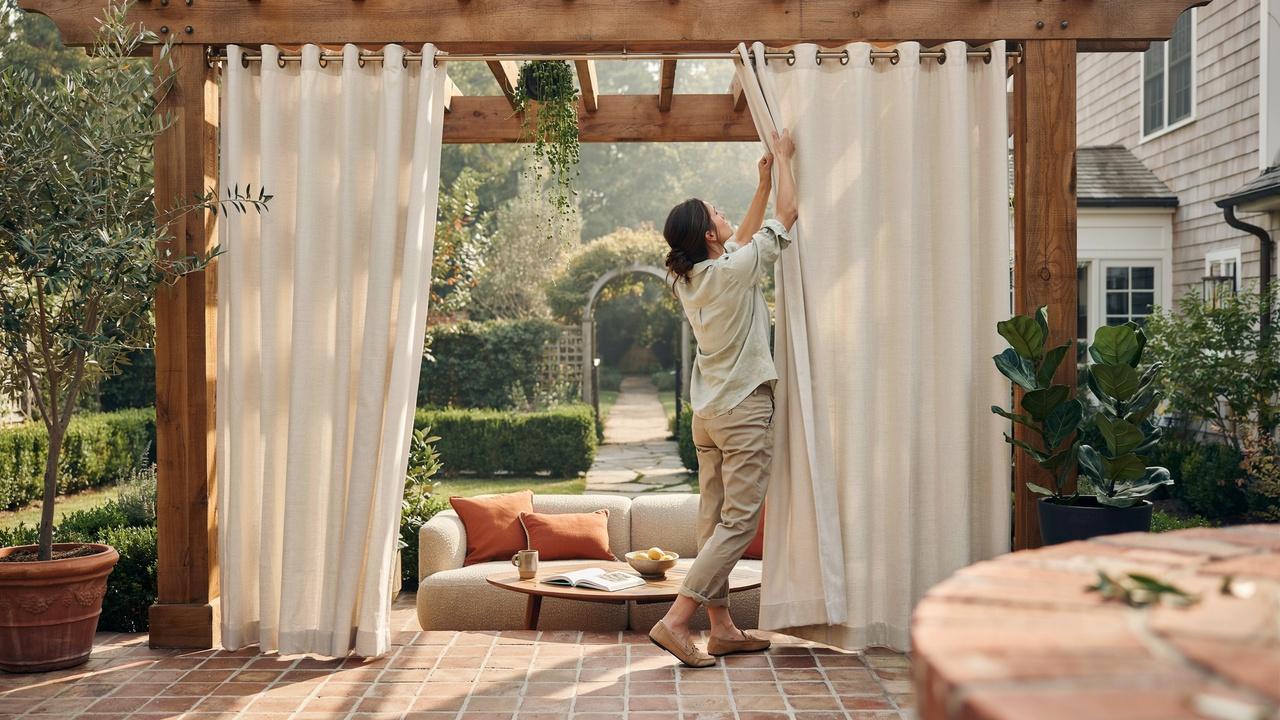 Homeowner installing outdoor curtains on a patio pergola in a modern backyard setting.
