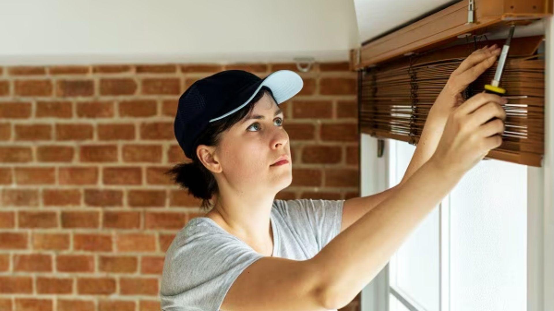 Person using screwdriver to loosen screws on headrail brackets while removing wood cellular shades