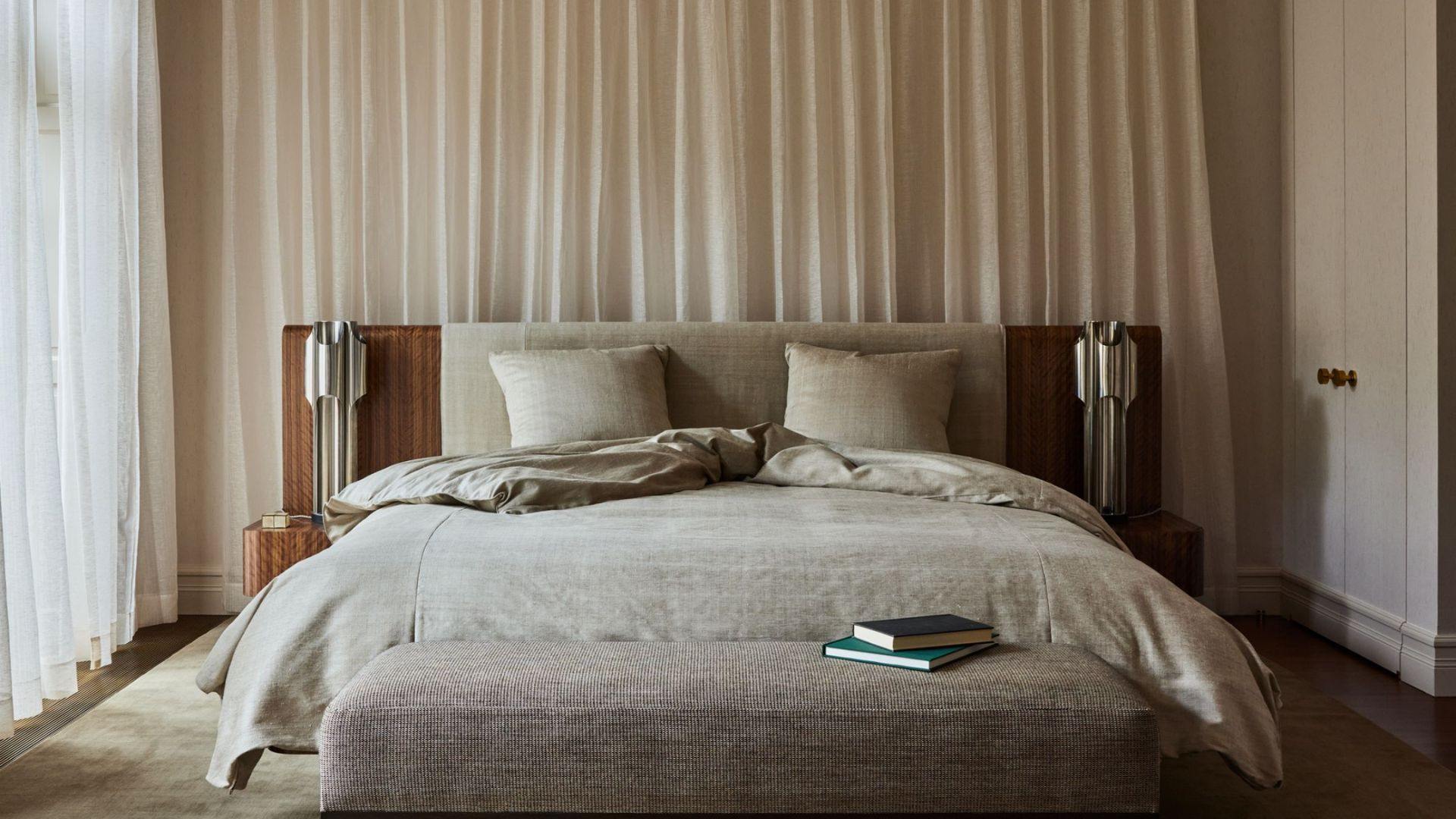 Cozy modern bedroom with beige upholstered bed, oak nightstands, pampas vase, glass doors with curtains.