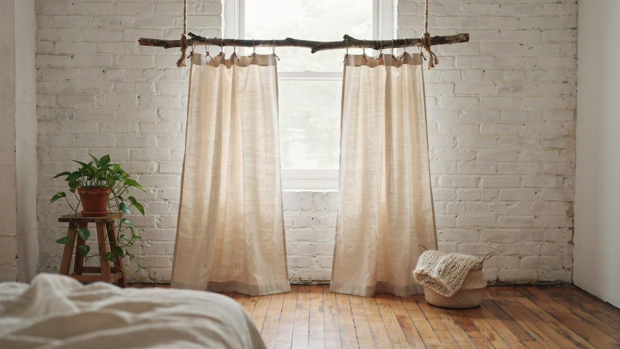 Natural branch curtain rod suspended from ceiling with rustic rope.