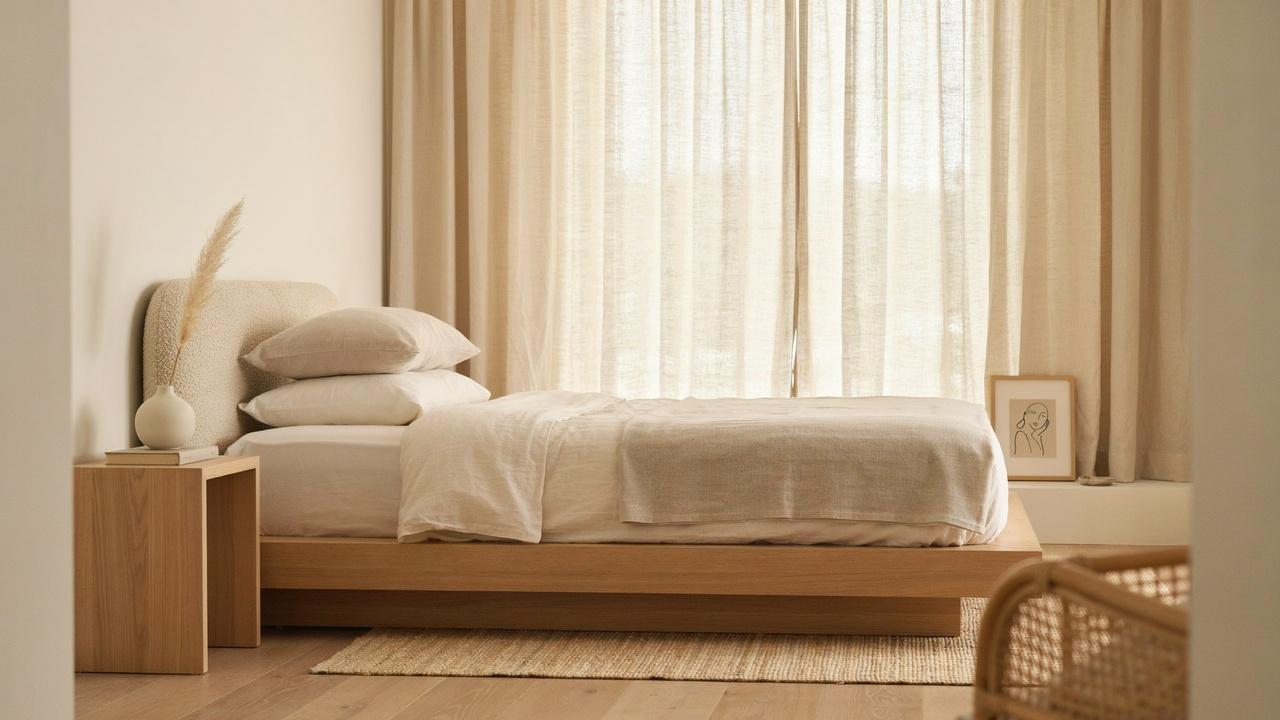Japandi bedroom with boucle platform bed, beige linen bedding, wood nightstand, sheer curtains, line art.