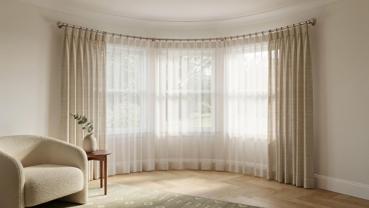 Curved curtain rod following the shape of a bay window with flowing curtains.