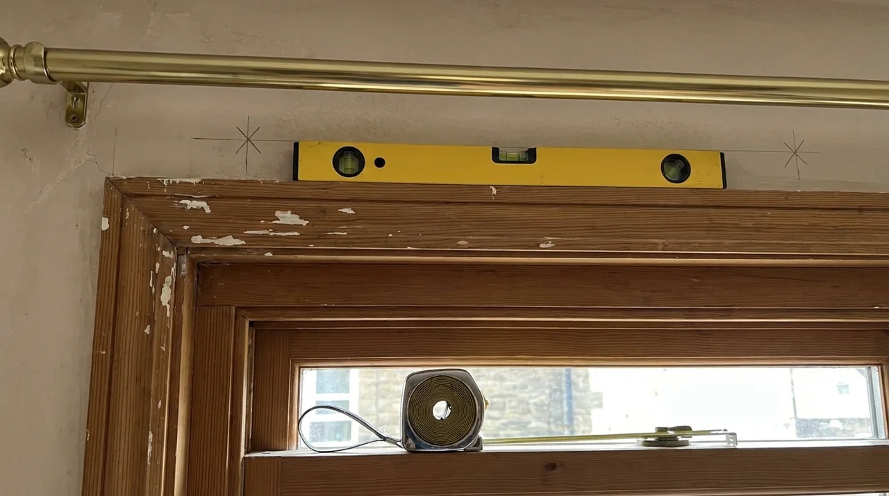Curtain rod bracket positions marked evenly above a window with a level and measuring tools.