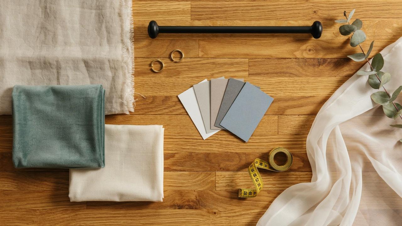 Flat lay of linen fabrics, paint swatches, black curtain rod, brass rings, measuring tape.