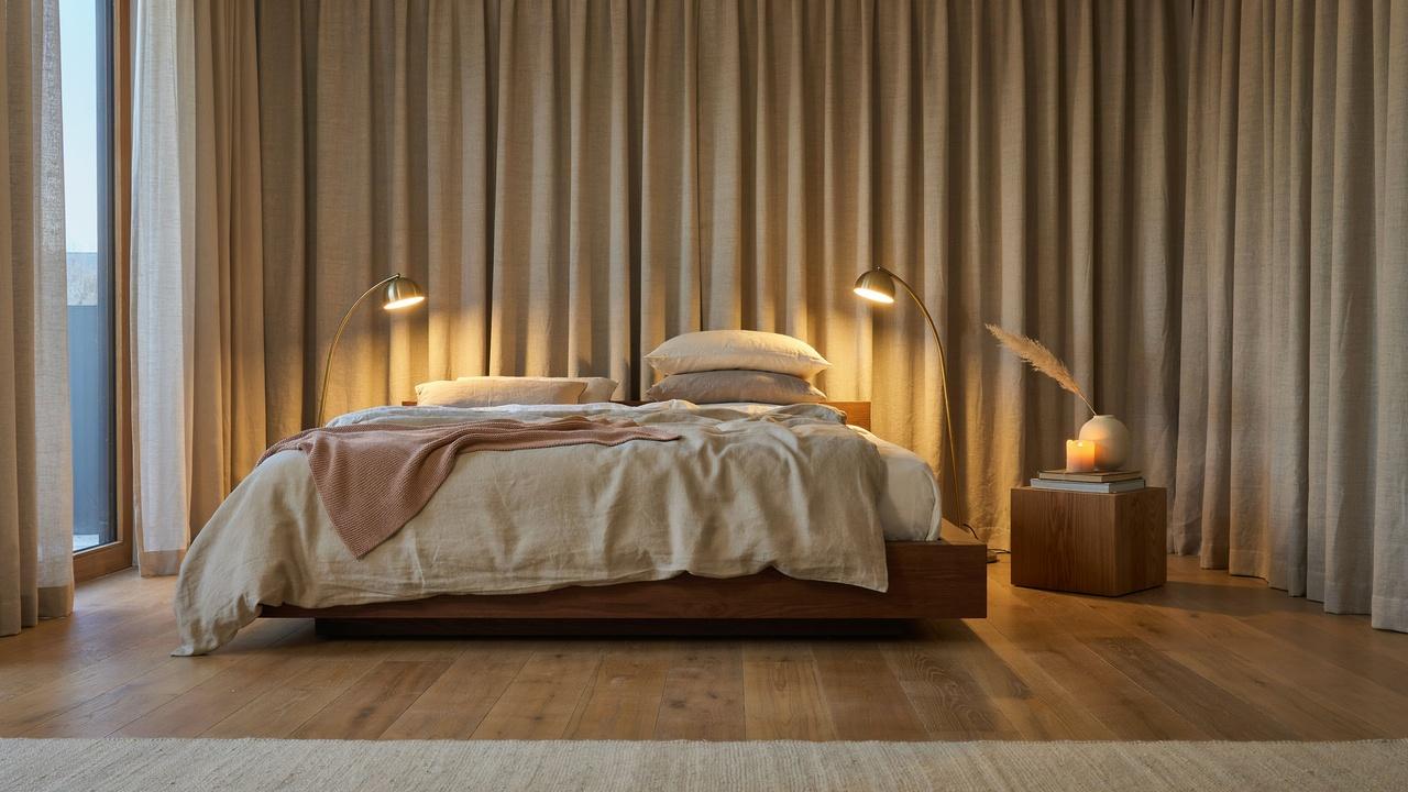Luxury minimalist bedroom with beige linen bed, wood headboard, chrome lamps, sheer curtains.