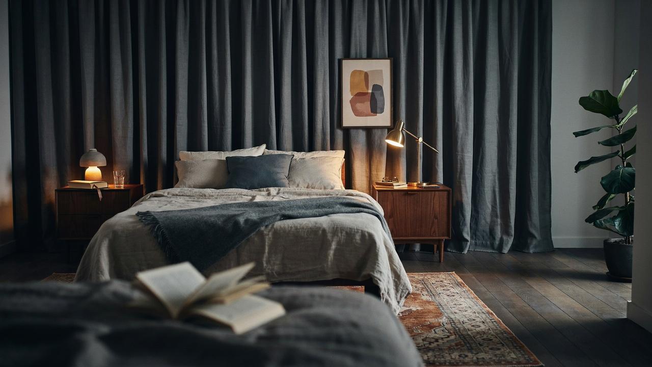 Dark moody bedroom with gray linen bedding, gray curtains, walnut nightstands, brass lamps, fiddle leaf fig.