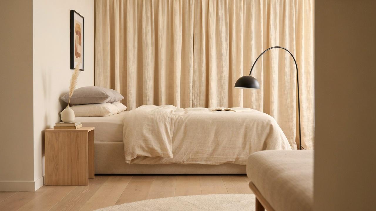 Minimal bedroom with beige platform bed, black arc floor lamp, beige linen curtains, wood side table.