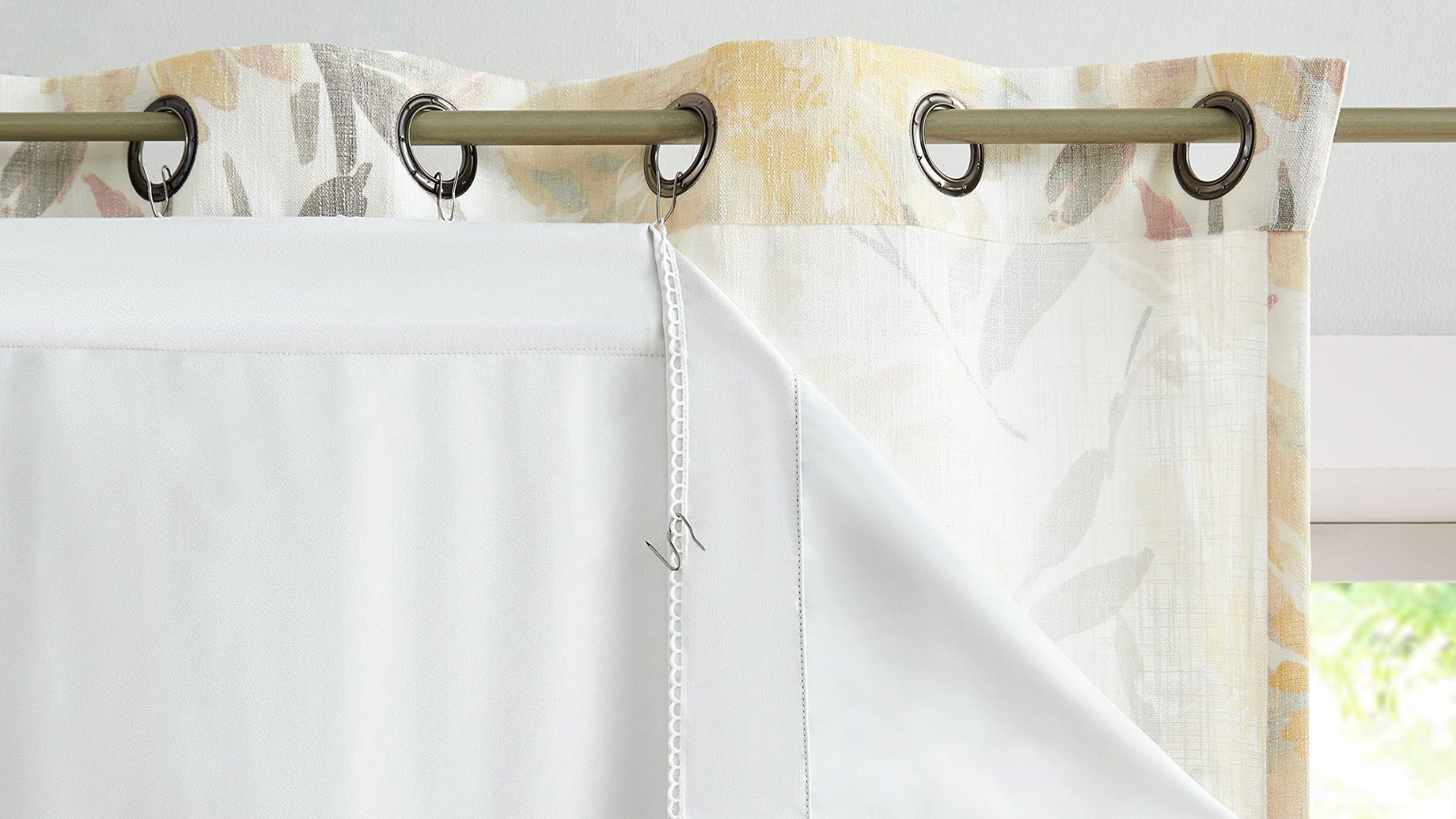 Close-up of floral grommet shower curtain with white waterproof liner attached via hooks on metal rod.